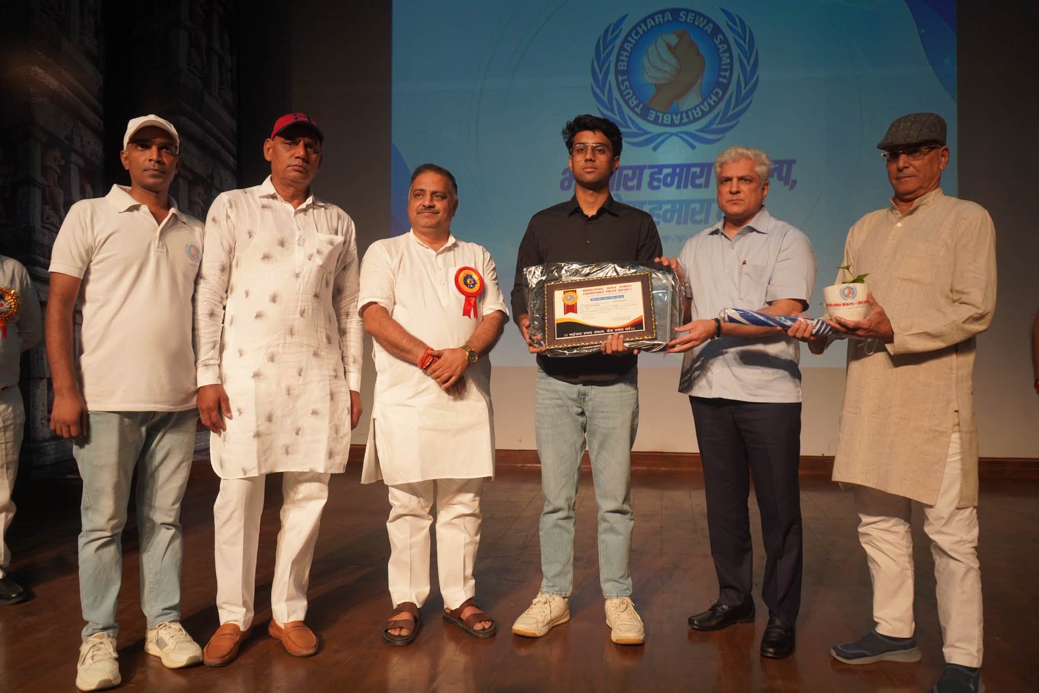 प्रतिभा सम्मान समारोह 2026 में मंच पर मेधावी छात्र को सम्मान-पत्र और पौधा भेंट करते अतिथि